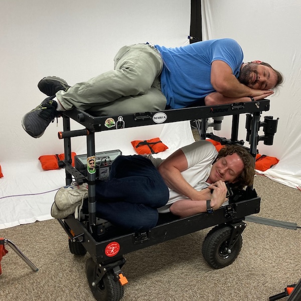 Two grown men cuddle up on a video production cart for an afternoon snooze.