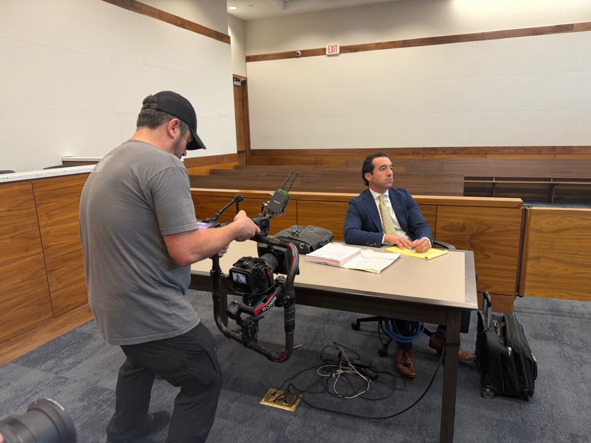 Camera operator filming Adam Funk in courtroom setting
