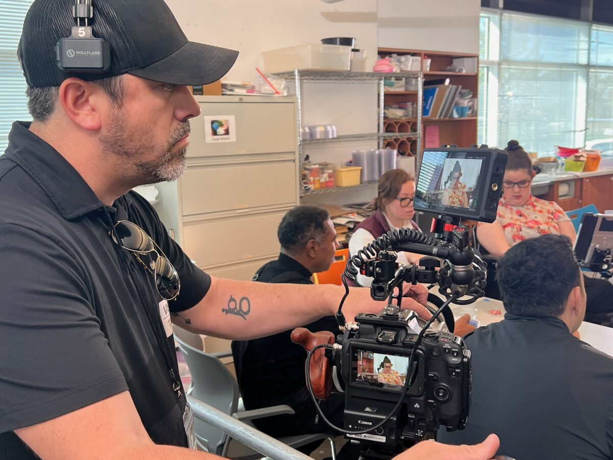 Behind the scenes of a man in a black hat filming a group of people sitting around a table for Cut To Create's project for Rice University's Kinder Institute for Urban Research