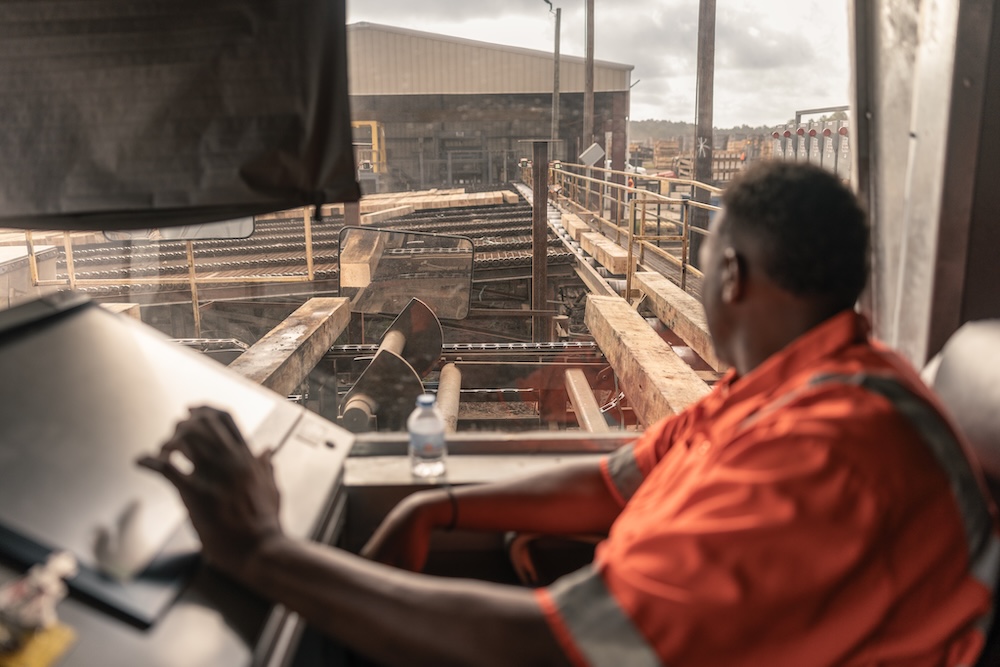 A worker sits at a computer while overlooking a timber yard.