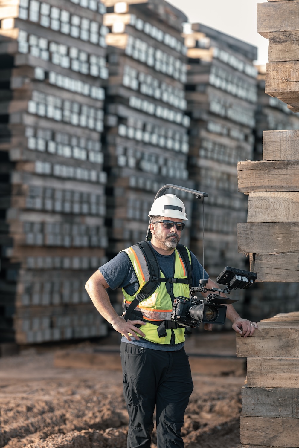 A camera operator leans on a pallet of wood